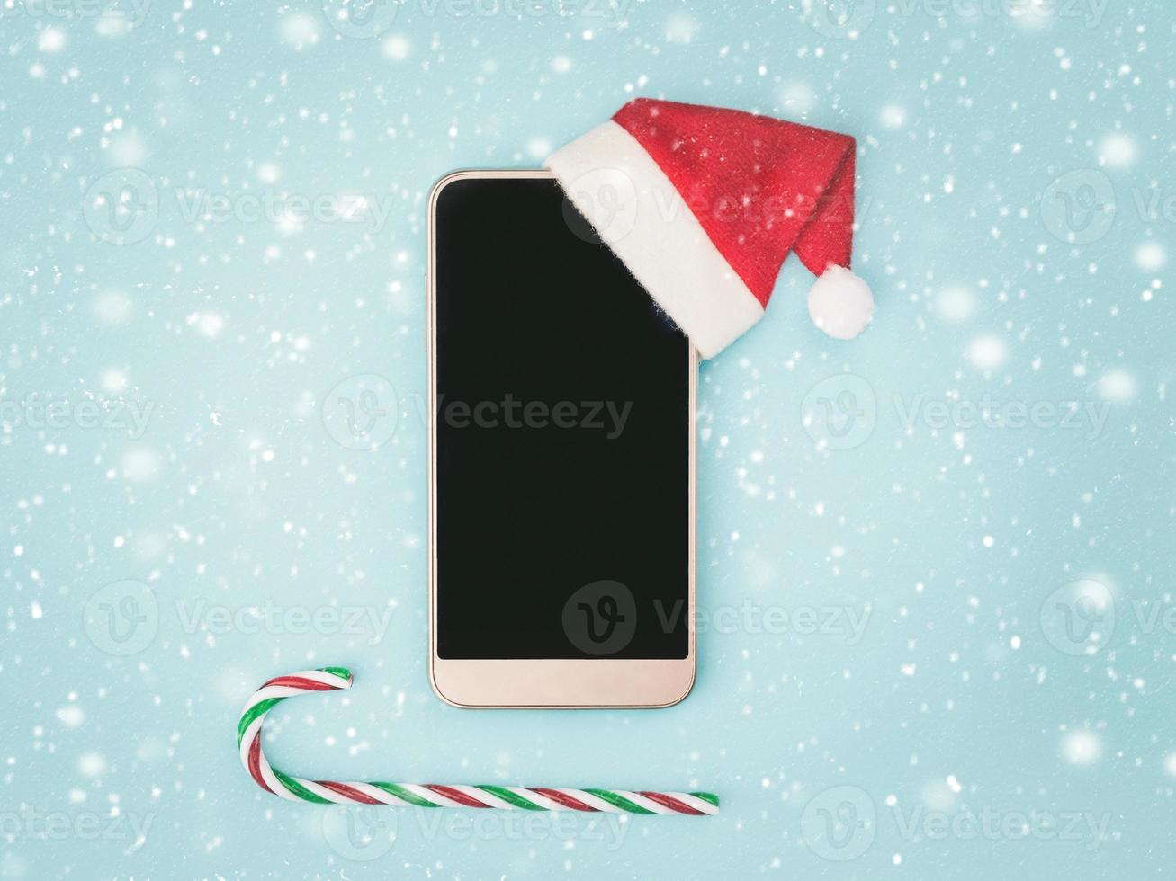 Christmas concept background.Smartphone with santa claus hat and caramel cane photo