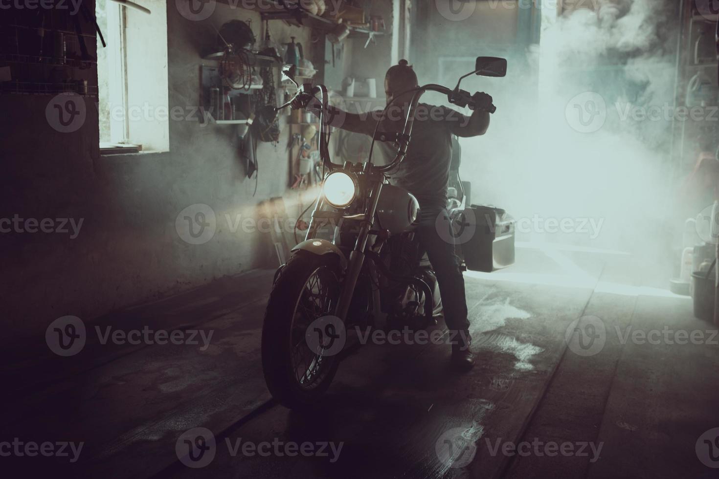 Handsome brutal man with a beard sitting on a motorcycle in his garage photo