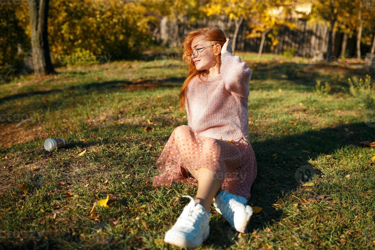 Portraits of a charming red-haired girl with a cute face. Girl posing in autumn park in a sweater and a coral-colored skirt. The girl has a wonderful mood photo
