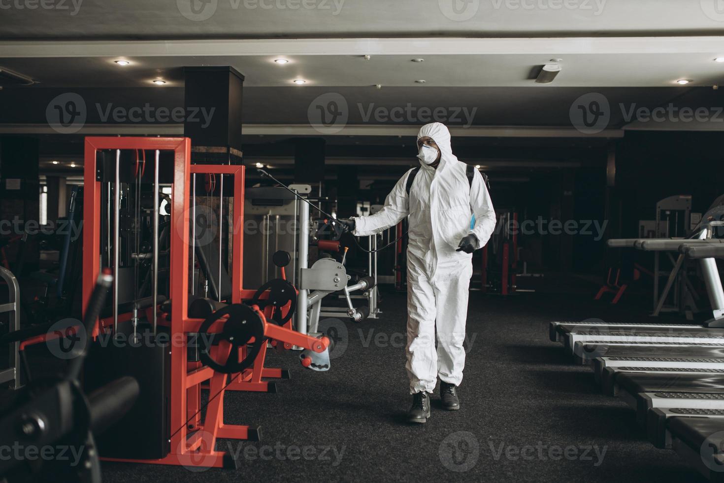 limpieza y desinfección en lugares concurridos en medio de la epidemia de coronavirus limpieza y desinfección de gimnasios prevención de infecciones y control de epidemias. traje de protección y máscara y bolsa de spray foto