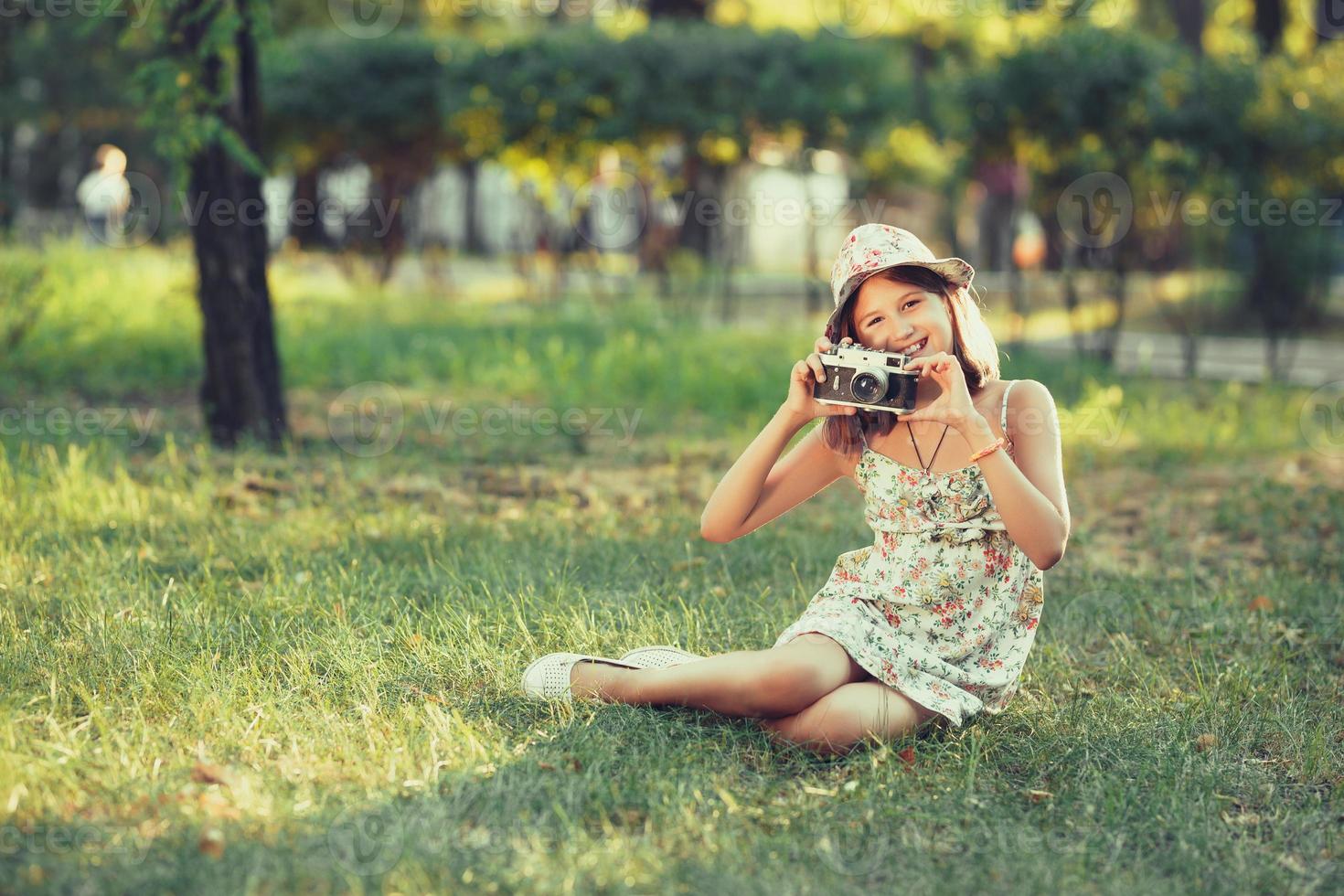 little girl is played by photo camera sitting on grass in park. Doing Selfie and photographing the world around