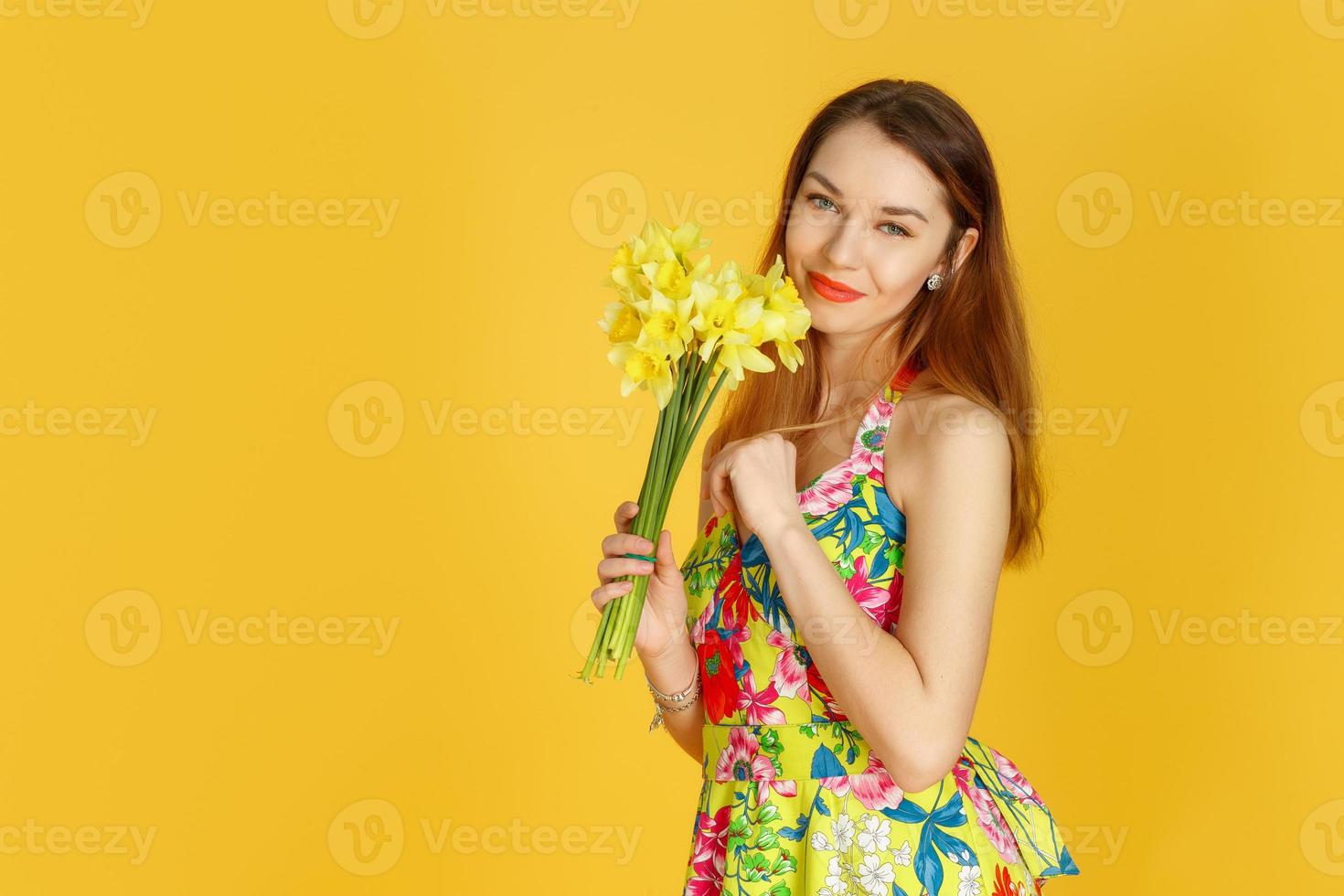 Young woman against yellow wall with flowers in hand photo