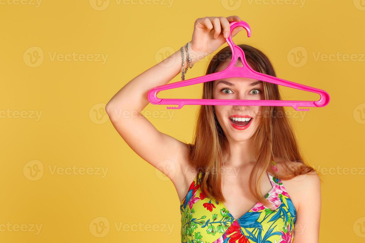 Young beautiful girl hides her face behind a clothes hanger. On a yellow background photo
