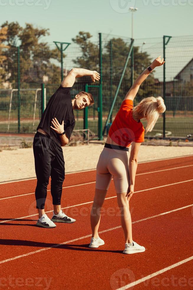 girl and a guy doing a warm-up before sports exercises at the school stadium photo
