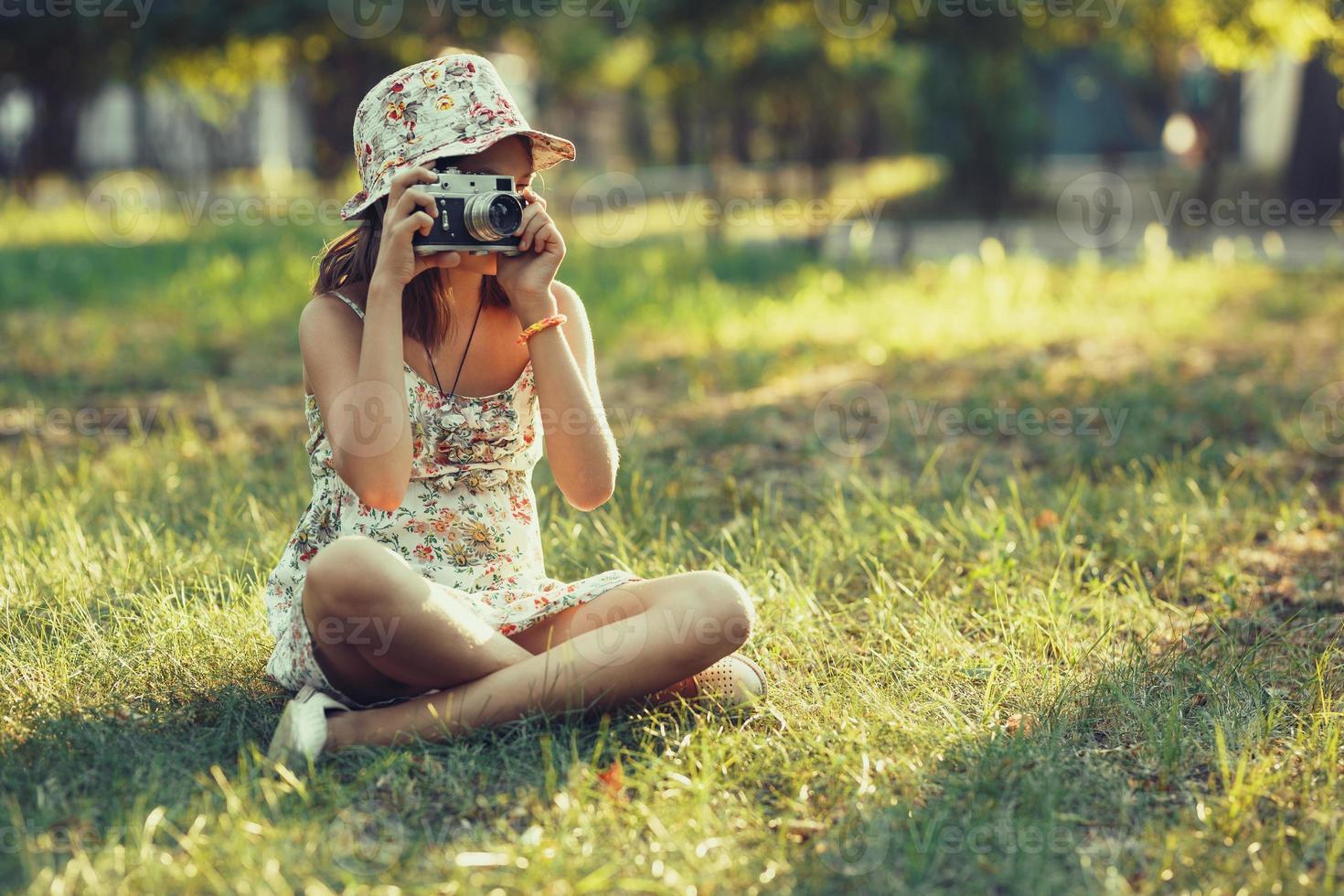 little girl is played by photo camera sitting on grass in park. Doing Selfie and photographing the world around