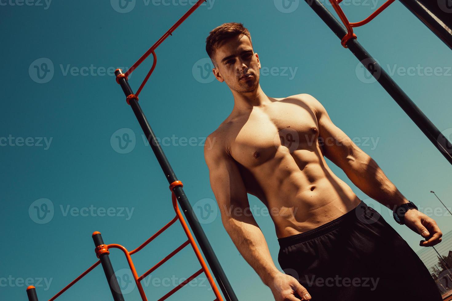 guy with a beautiful athletic body posing while standing next to the horizontal bars photo