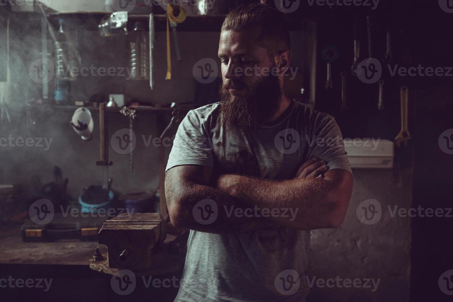 Handsome brutal man with a beard standing in his garage against the background of repair tools photo