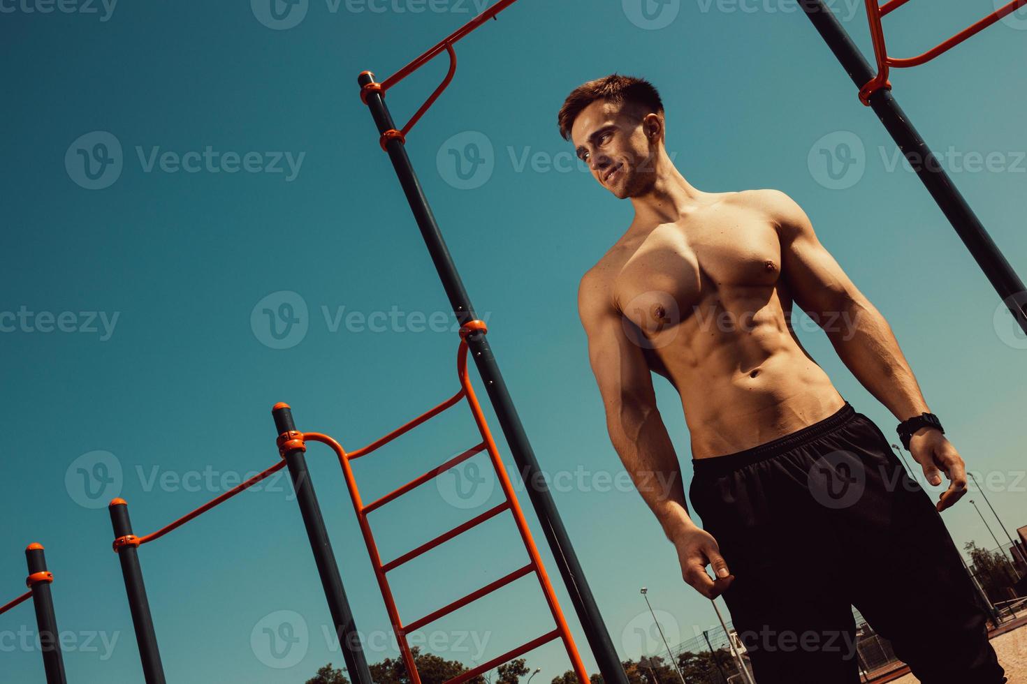 guy with a beautiful athletic body posing while standing next to the horizontal bars photo