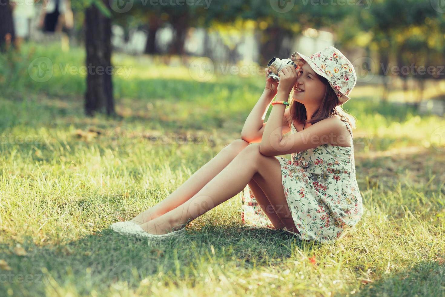 little girl is played by photo camera sitting on grass in park. Doing Selfie and photographing the world around