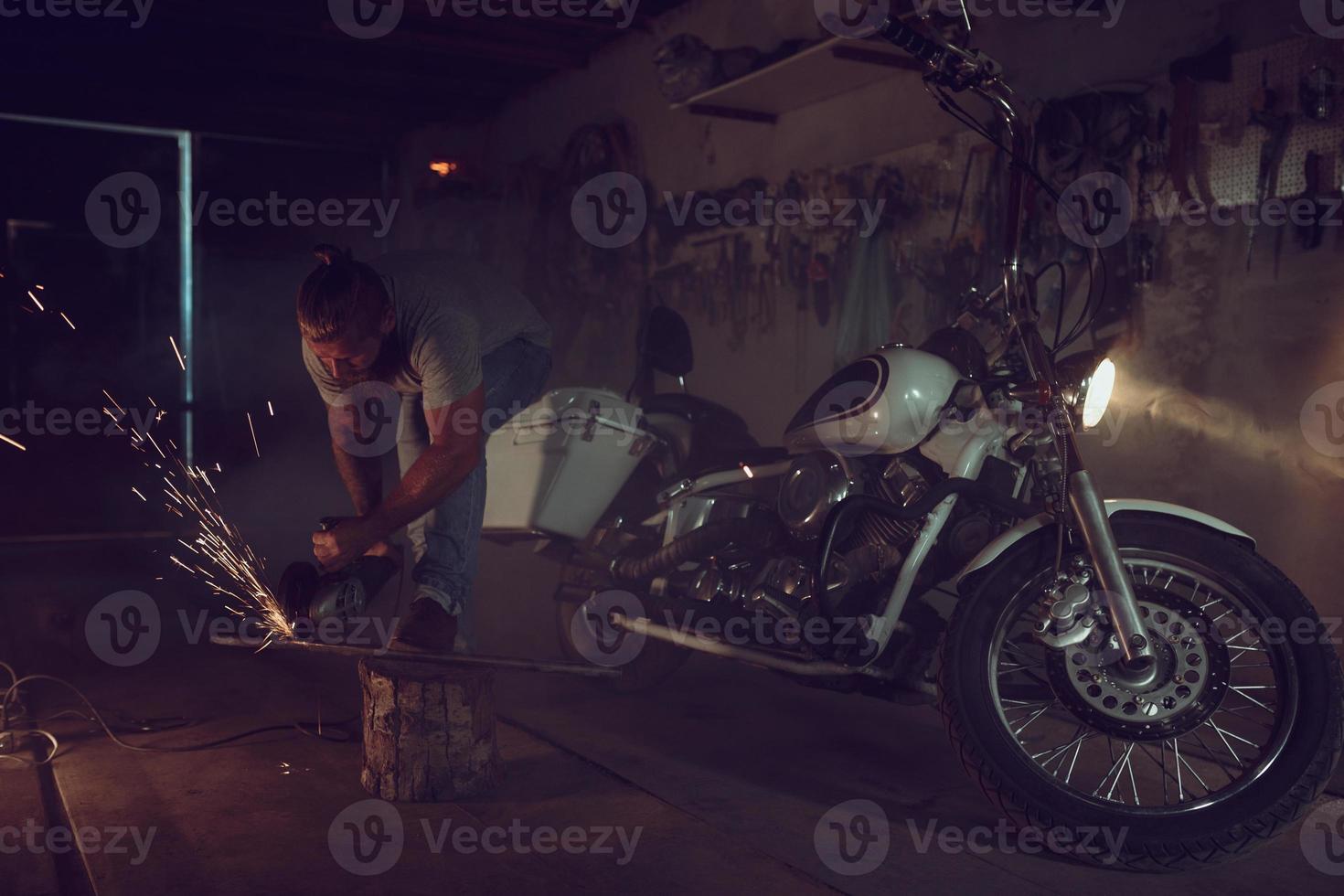 Handsome brutal male with a beard repairing a motorcycle in his garage working with a circular saw. In the garage a lot of sparks and smoke from sawing photo