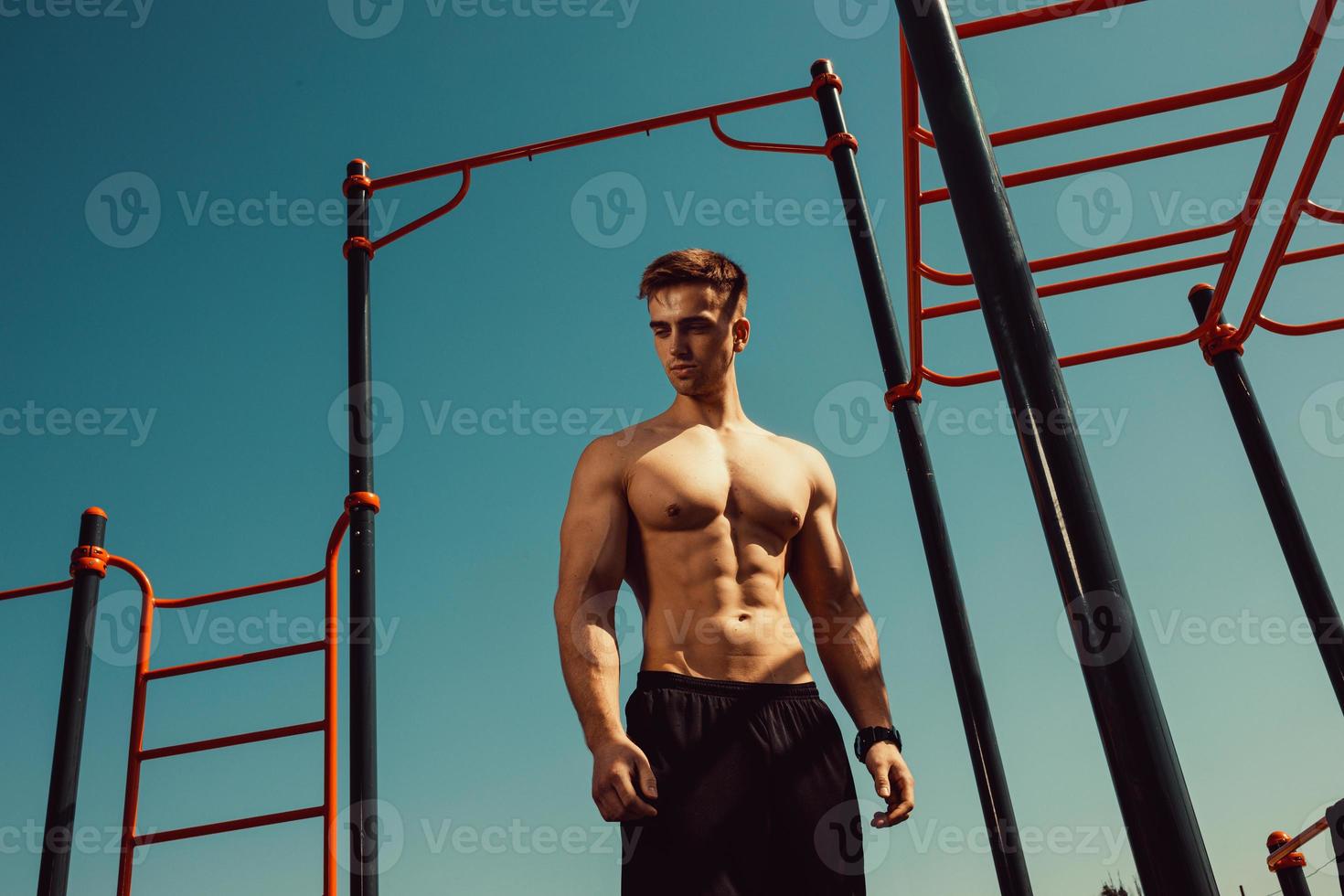 guy with a beautiful athletic body posing while standing next to the horizontal bars photo