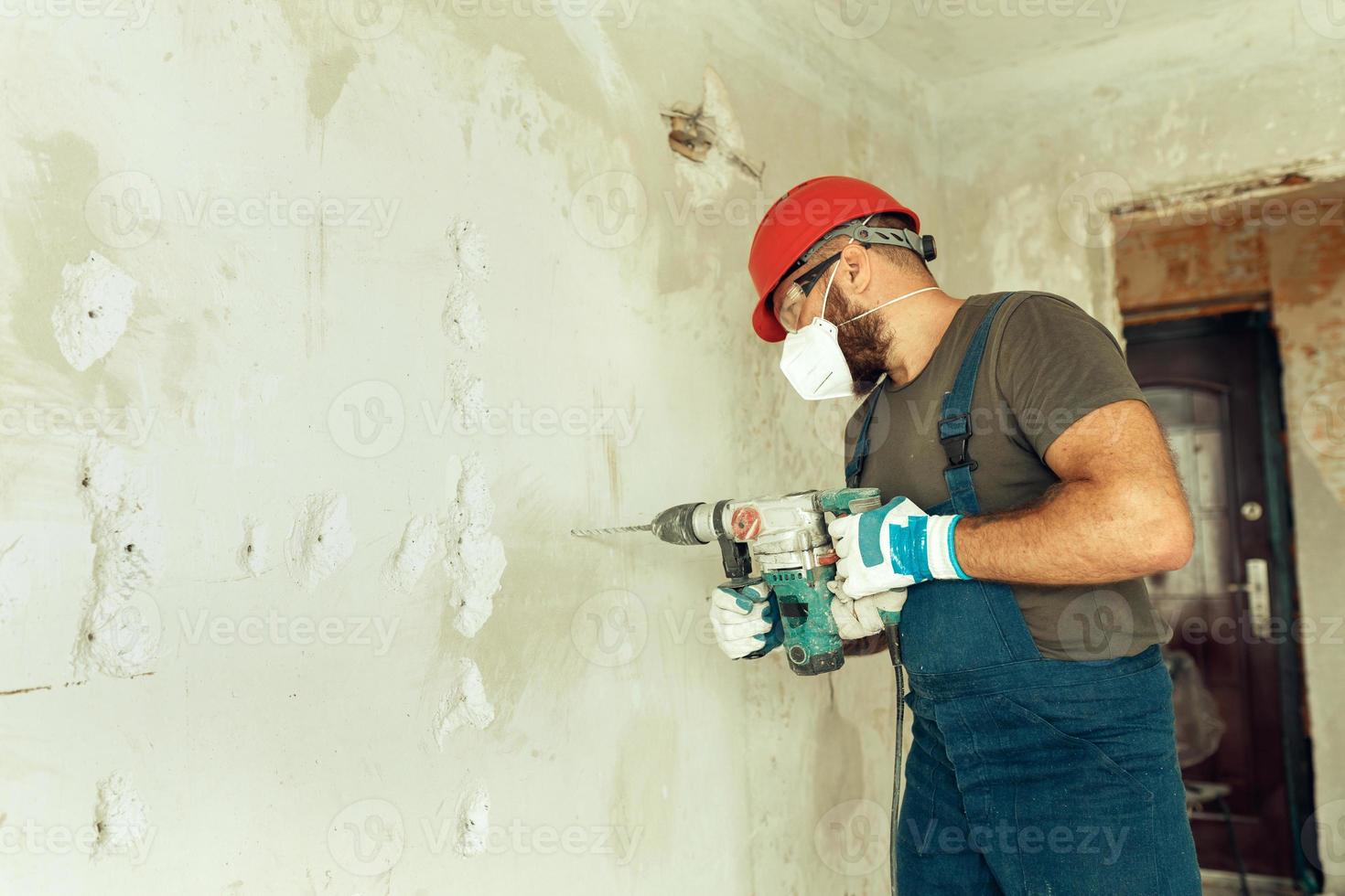 builder with perforator drills holes in concrete wall photo