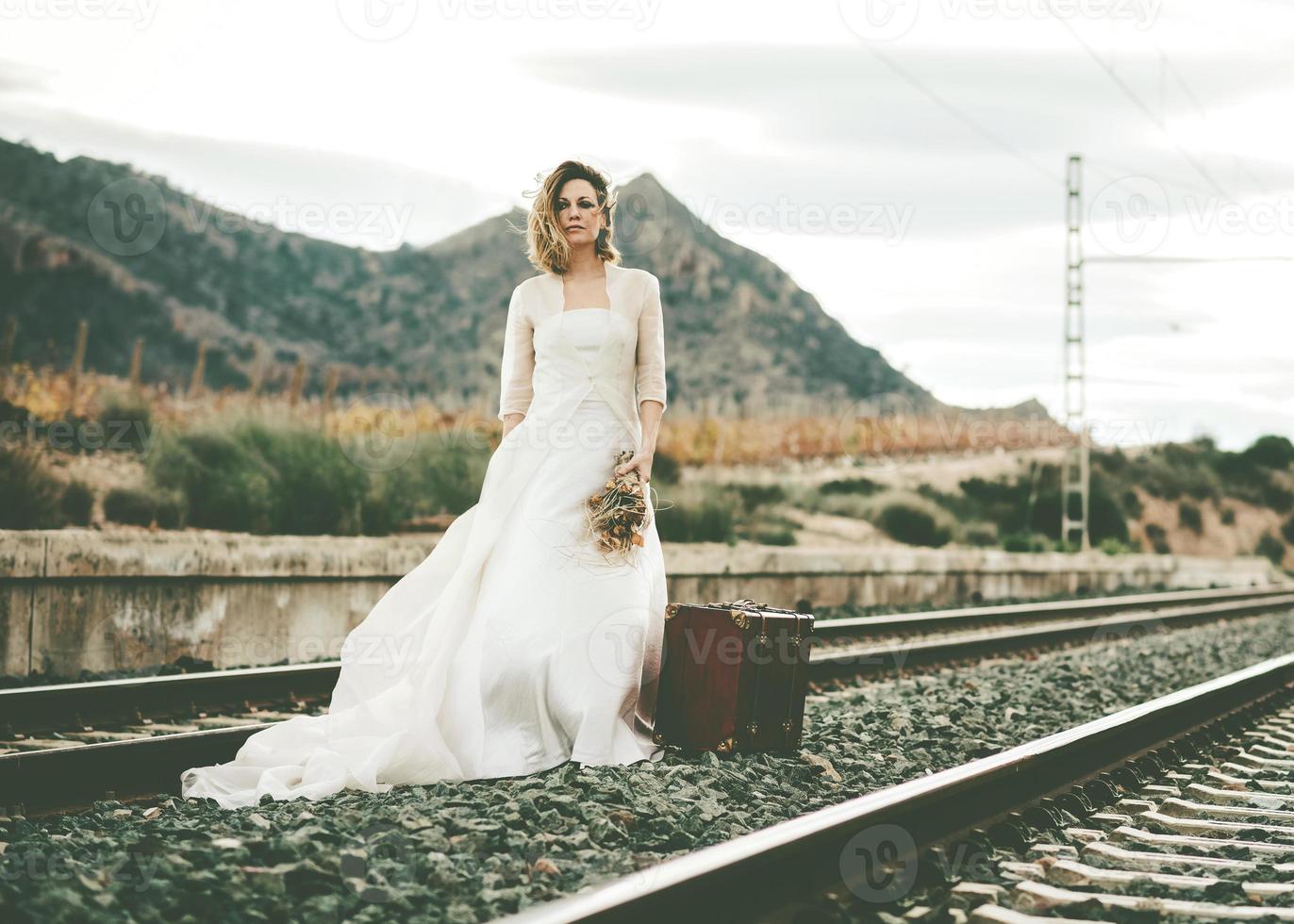 bride with a red suitcase on the train tracks photo