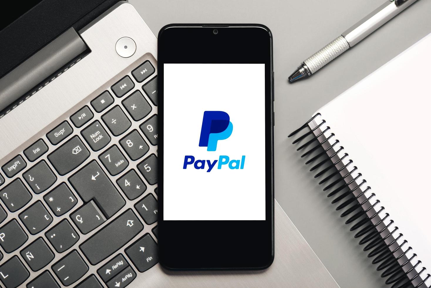 Paypal logo on black screen of smartphone with laptop and notebook photo