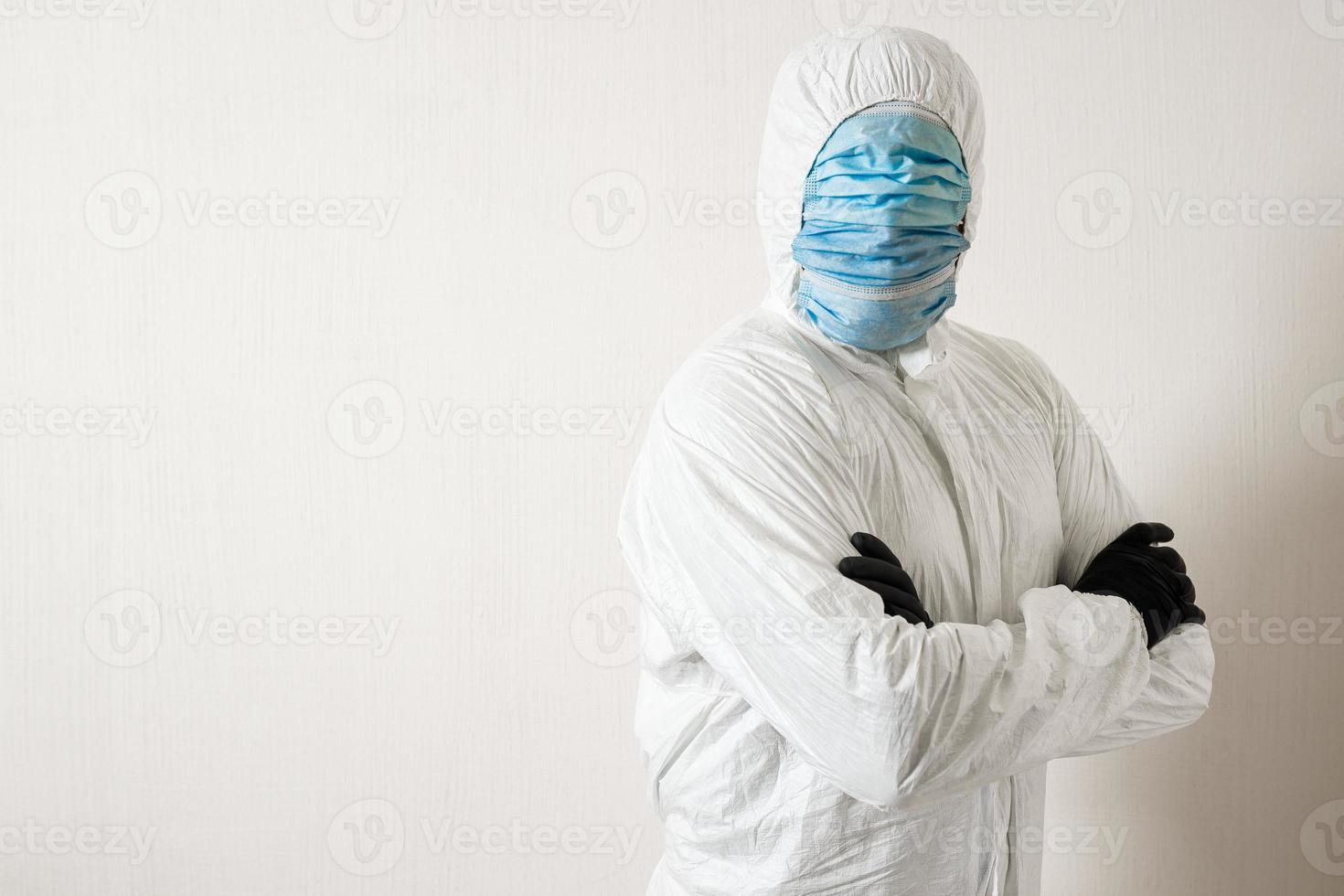 a man in a protective suit hung with medical masks posing against a wall background showing various gestures with his fingers photo