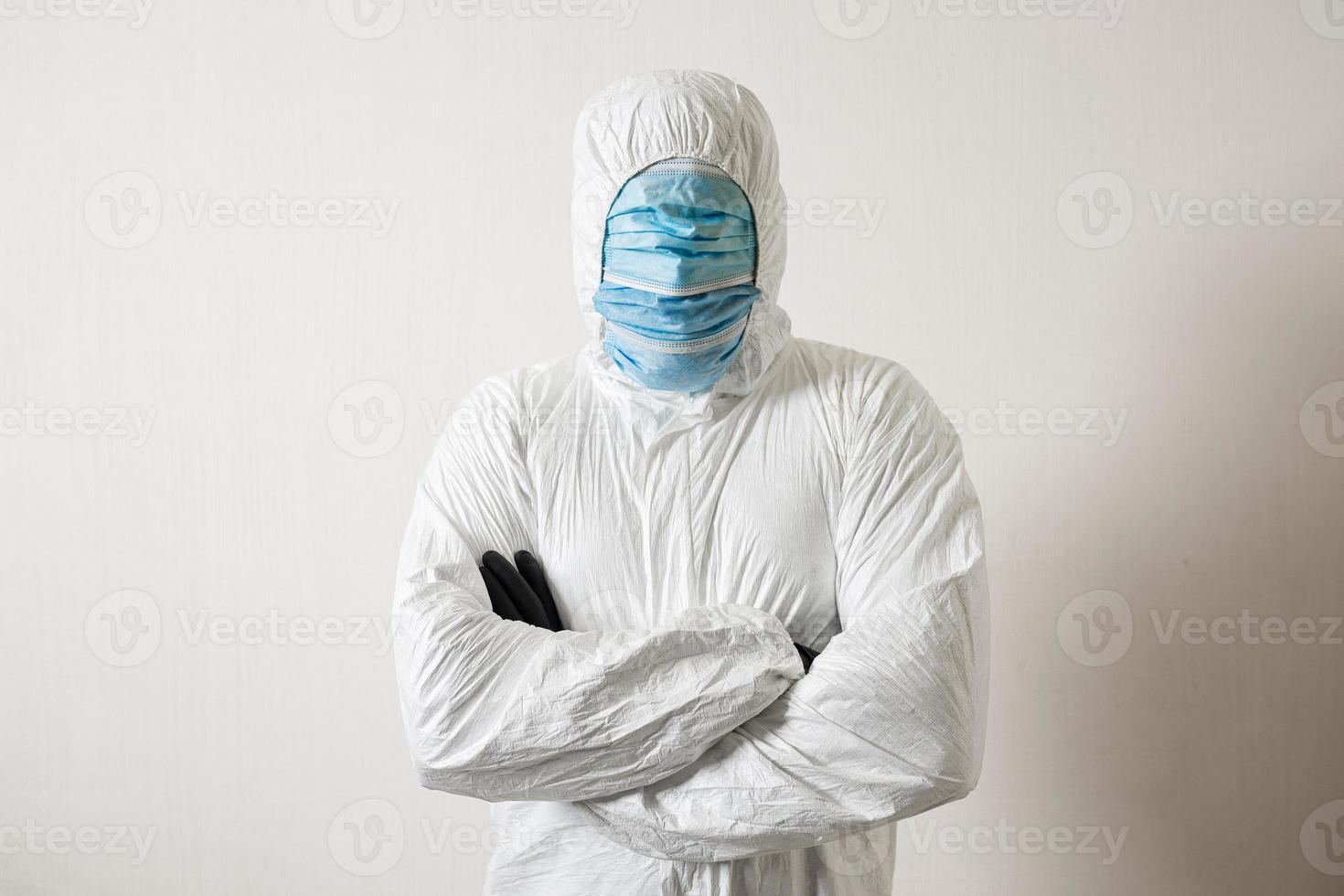 a man in a protective suit hung with medical masks posing against a wall background showing various gestures with his fingers photo