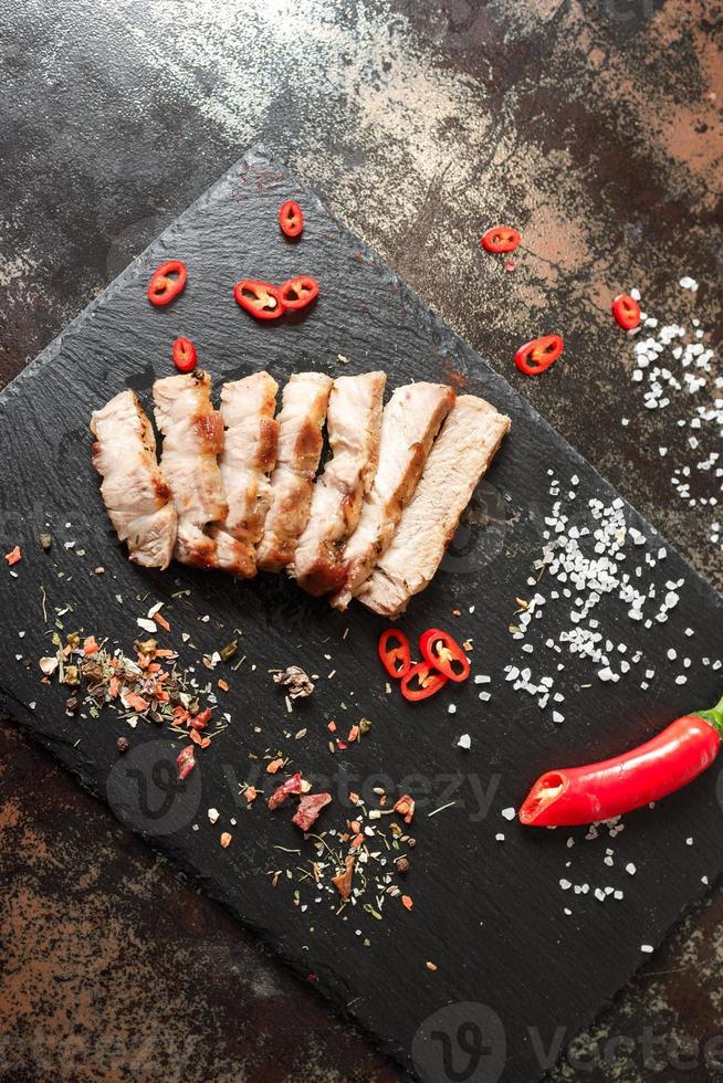 pork cooked in a pan and cut into pieces with spices on a dark stone background photo