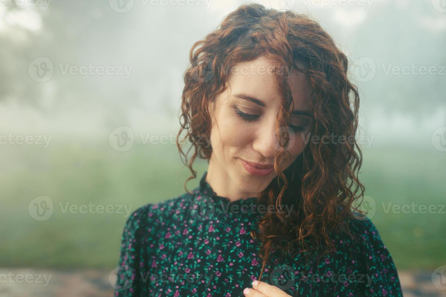 cute red-haired curly girl rejoices under the water fogger in the city center photo