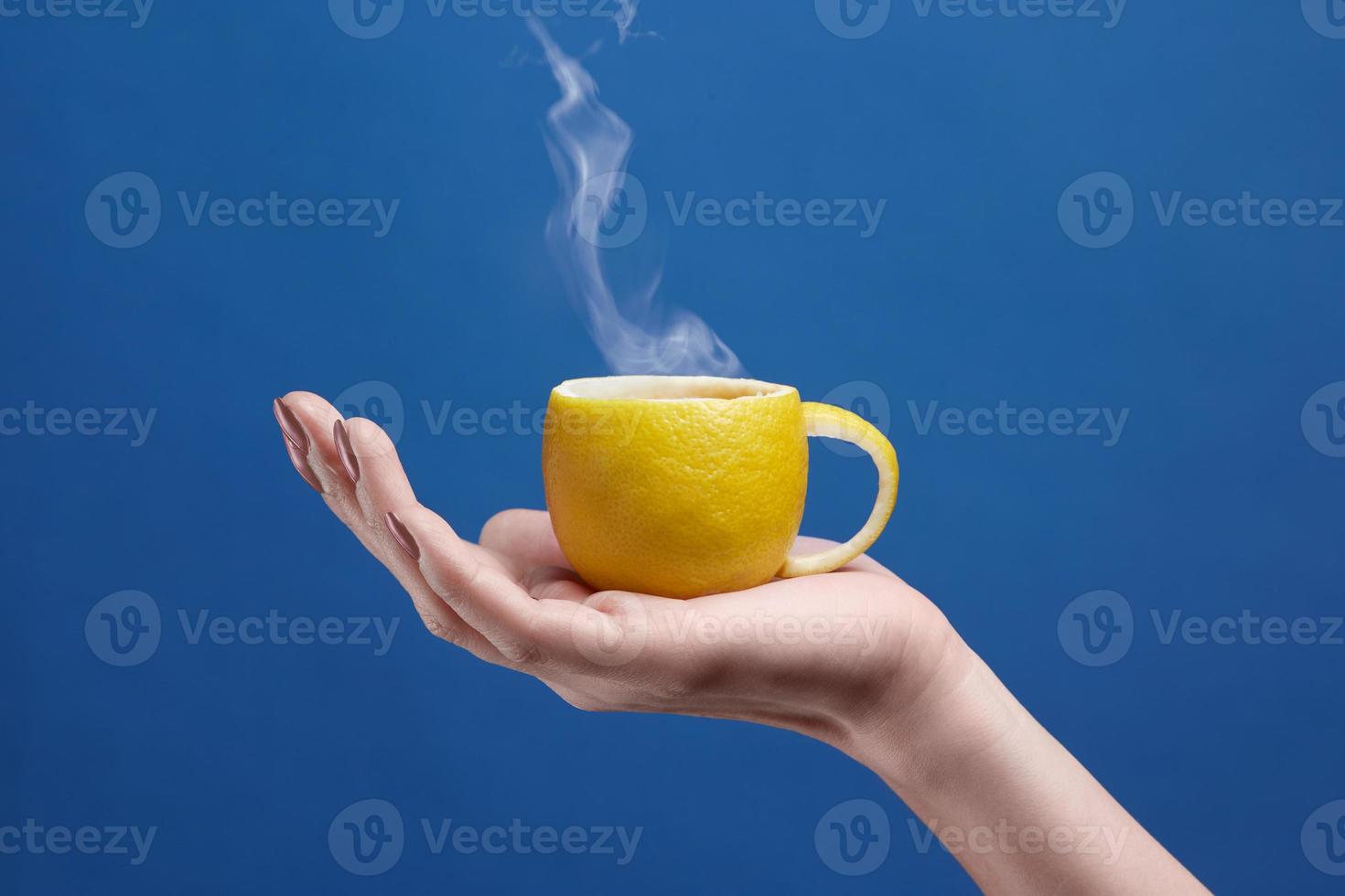 una taza de té hecha de limón. taza de limón en la mano sobre un fondo azul. composición creativa sobre el tema del té de frutas naturales. foto