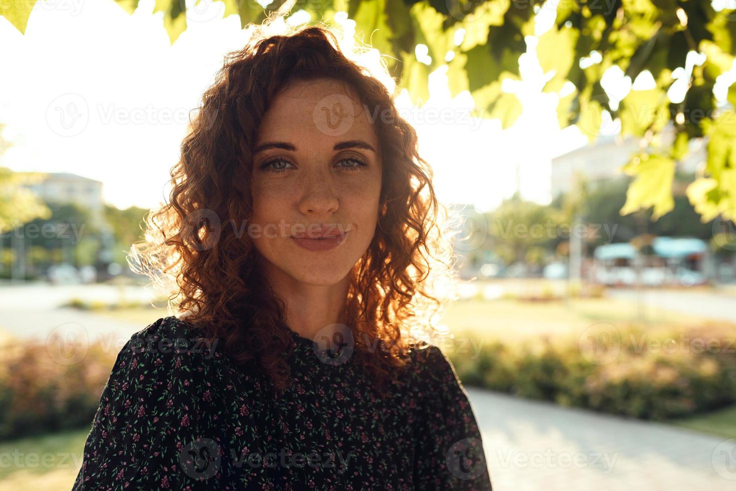 Portraits of a charming red-haired girl with freckles and a pretty face. The girl poses for the camera in the city center. She has a great mood and a sweet smile photo