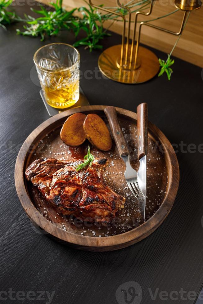bistec medio raro sobre costilla de ternera con patatas en un plato de madera foto