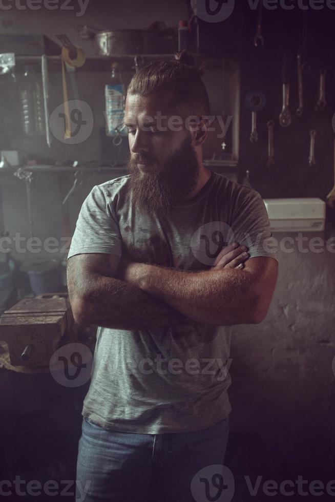 apuesto hombre brutal con barba parado en su garaje contra el fondo de herramientas de reparación foto