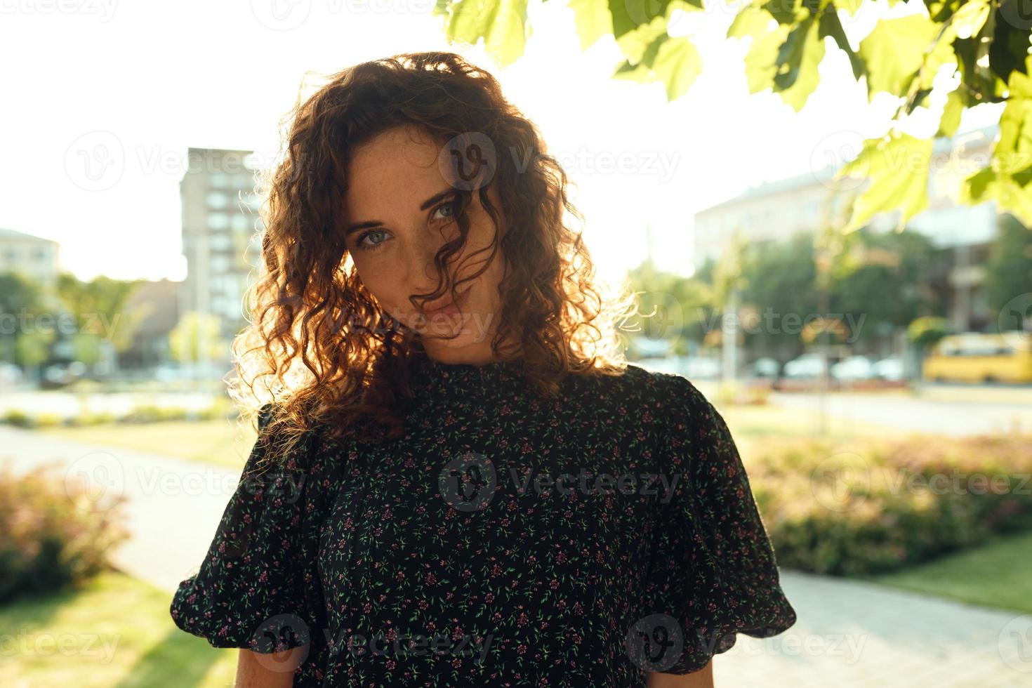 Portraits of a charming red-haired girl with freckles and a pretty face. The girl poses for the camera in the city center. She has a great mood and a sweet smile photo