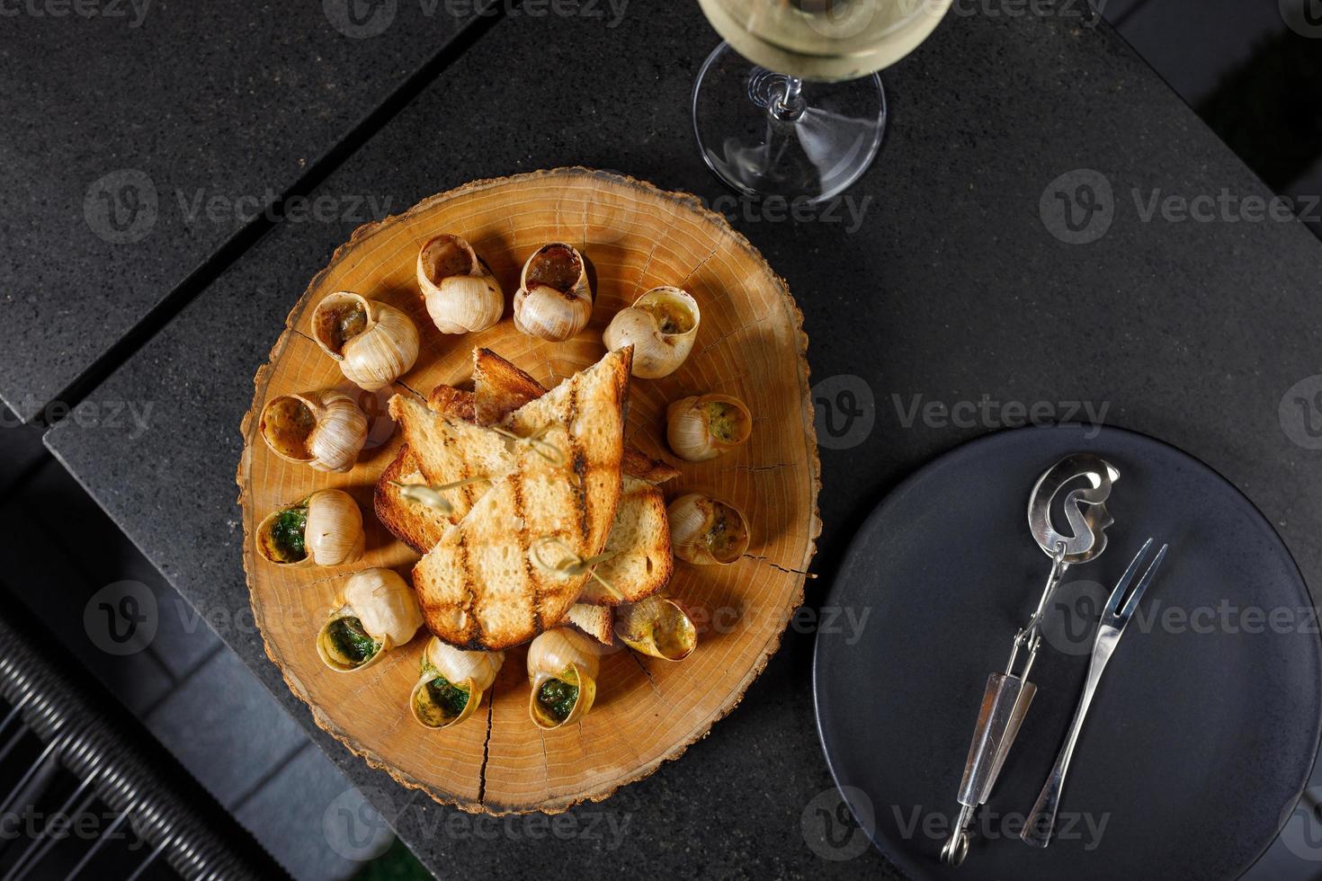 Baked snails with garlic oil and herbs on a wooden plank photo