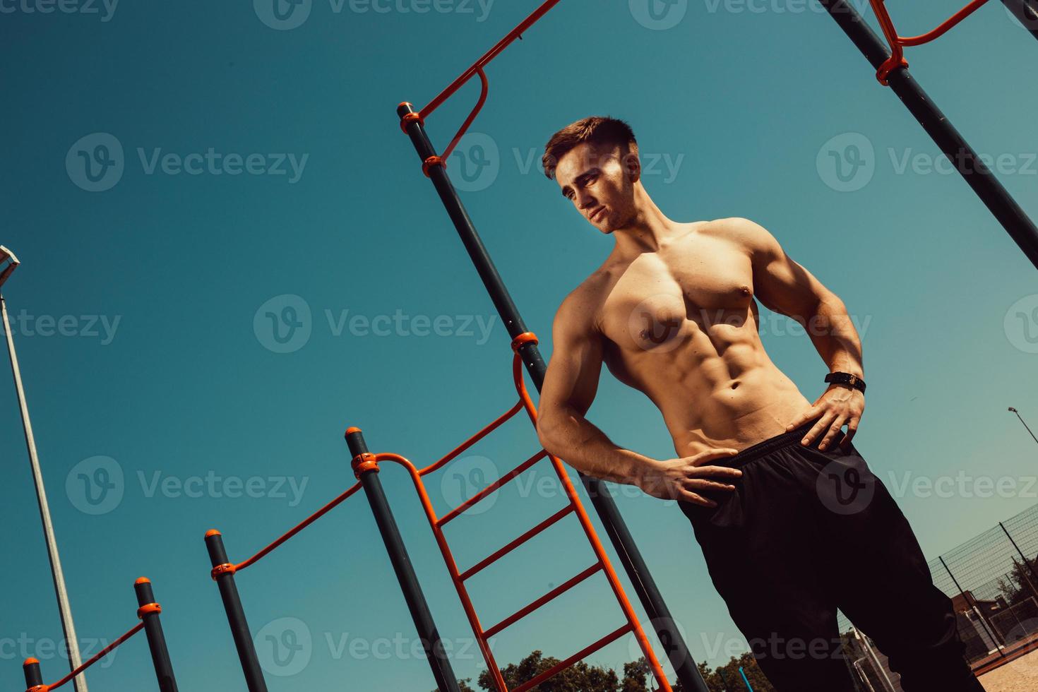 guy with a beautiful athletic body posing while standing next to the horizontal bars photo