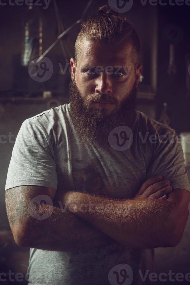 Handsome brutal man with a beard standing in his garage against the background of repair tools photo