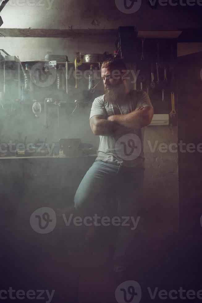 Handsome brutal man with a beard standing in his garage against the background of repair tools photo