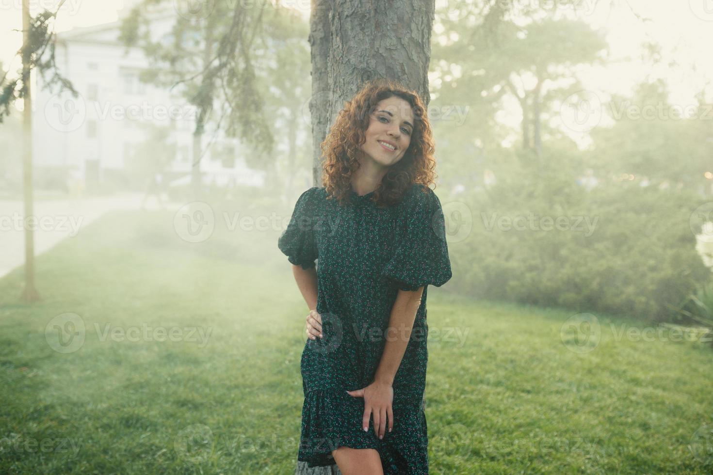 cute red-haired curly girl rejoices under the water fogger in the city center photo