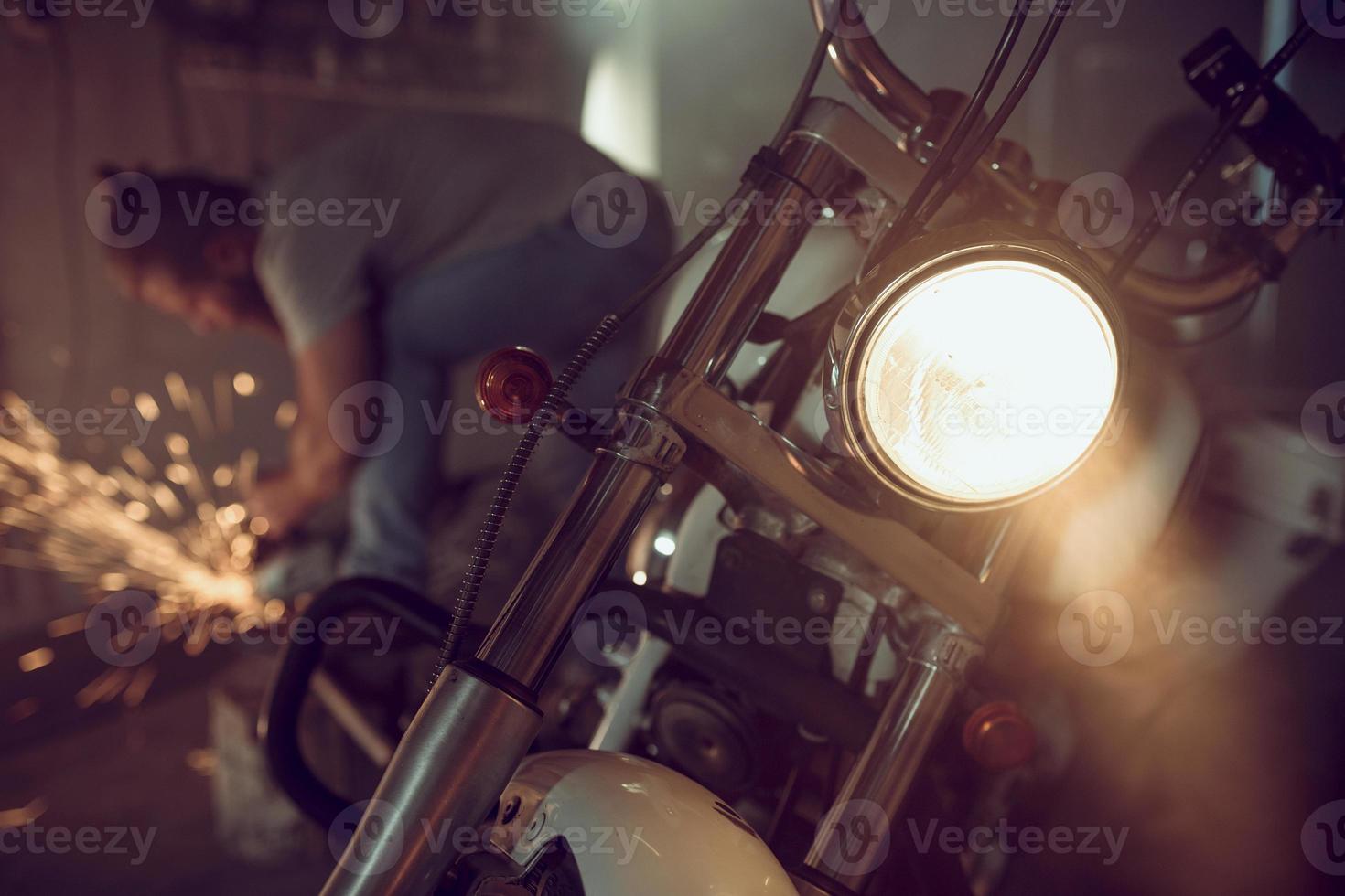 apuesto hombre brutal con barba reparando una motocicleta en su garaje trabajando con una sierra circular. en el garaje muchas chispas y humo de aserrar foto