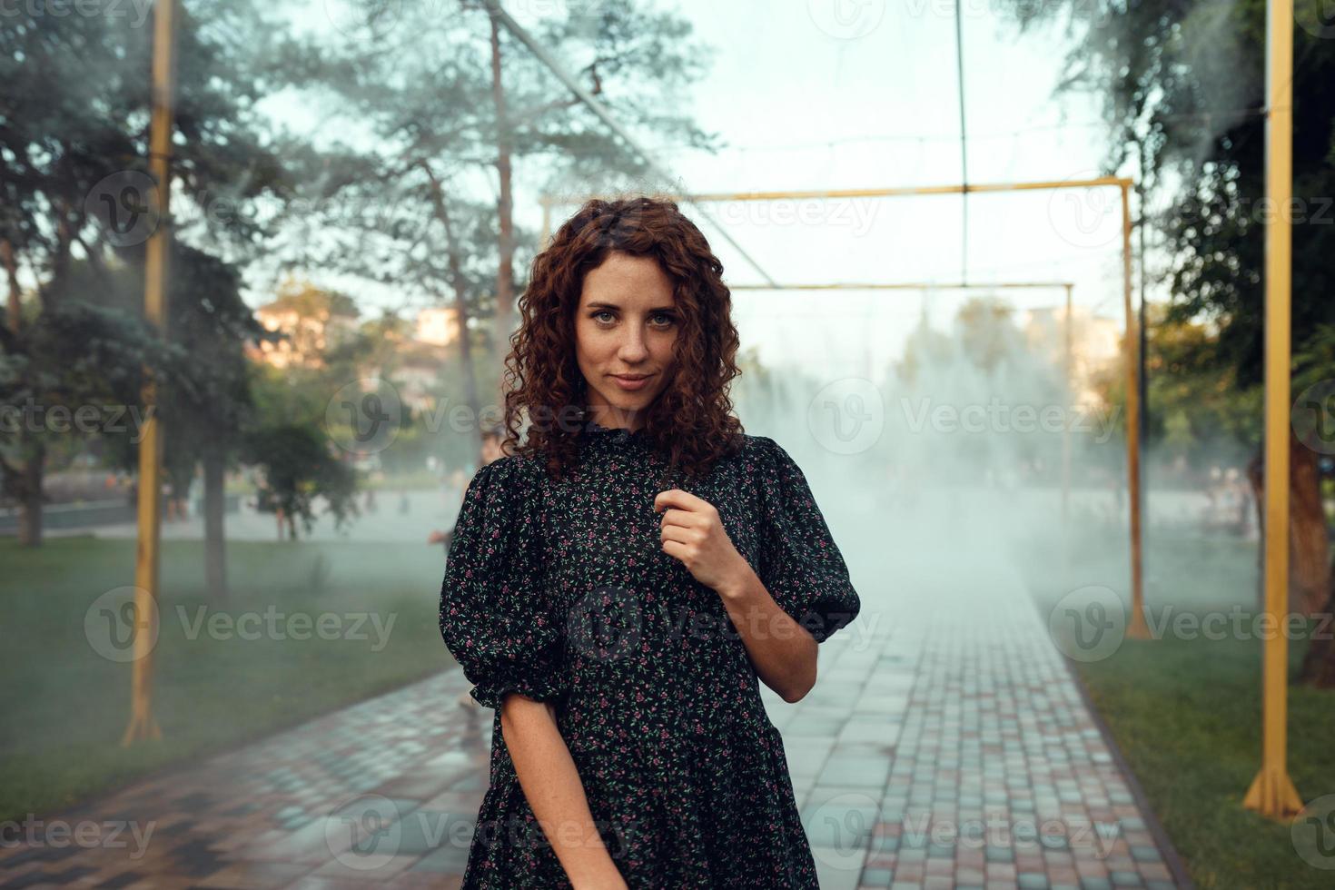 cute red-haired curly girl rejoices under the water fogger in the city center photo