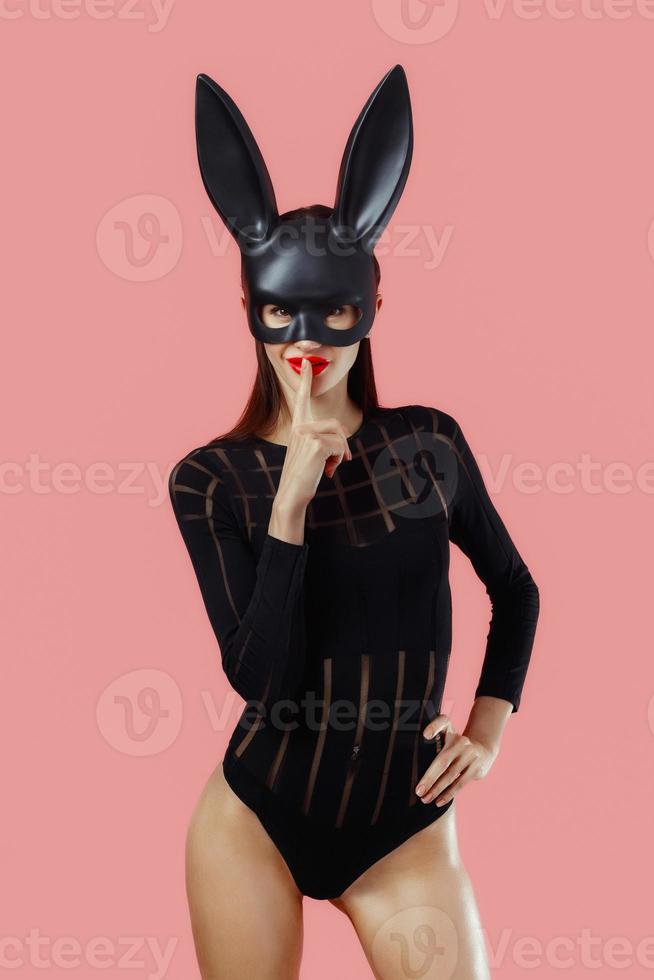 Sexy woman wearing a black mask Easter bunny standing on a pink background and looks very sensually photo