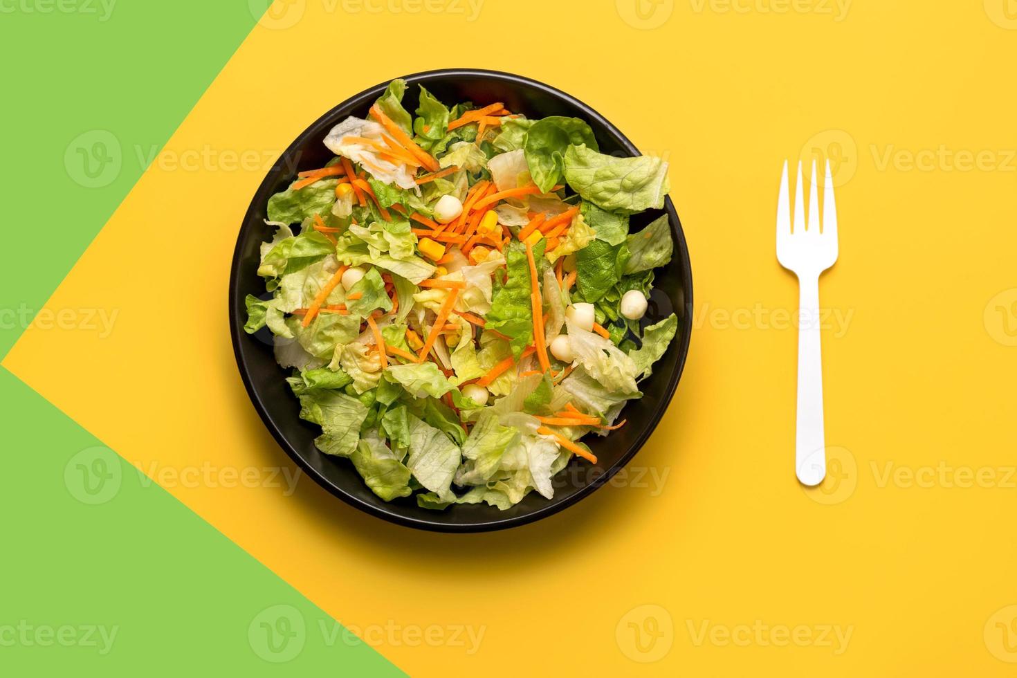 ensalada de lechuga con zanahoria, maíz y queso y tenedor blanco. concepto de comida saludable foto