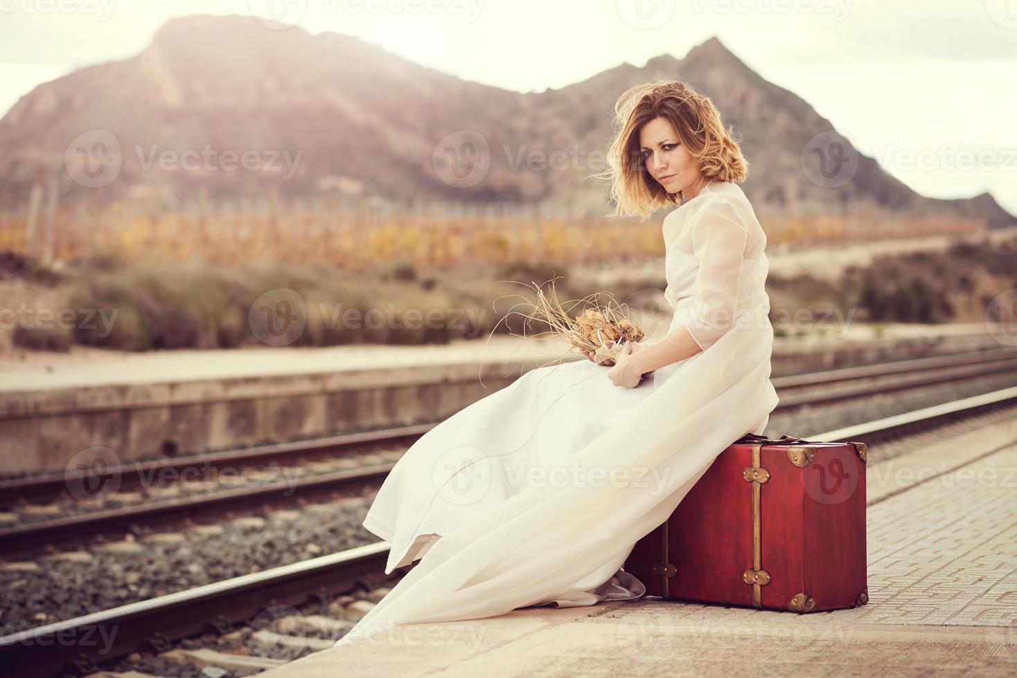 novia pensativa con una maleta roja en las vías del tren foto