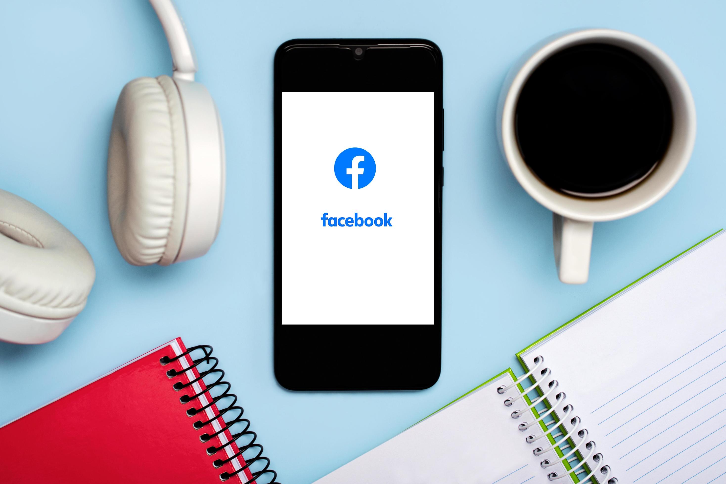 Facebook logo on white screen of smartphone with notebooks,headphone