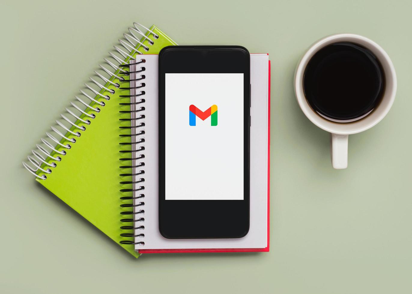 logotipo de gmail en la pantalla negra del teléfono inteligente con cuadernos y taza de café foto