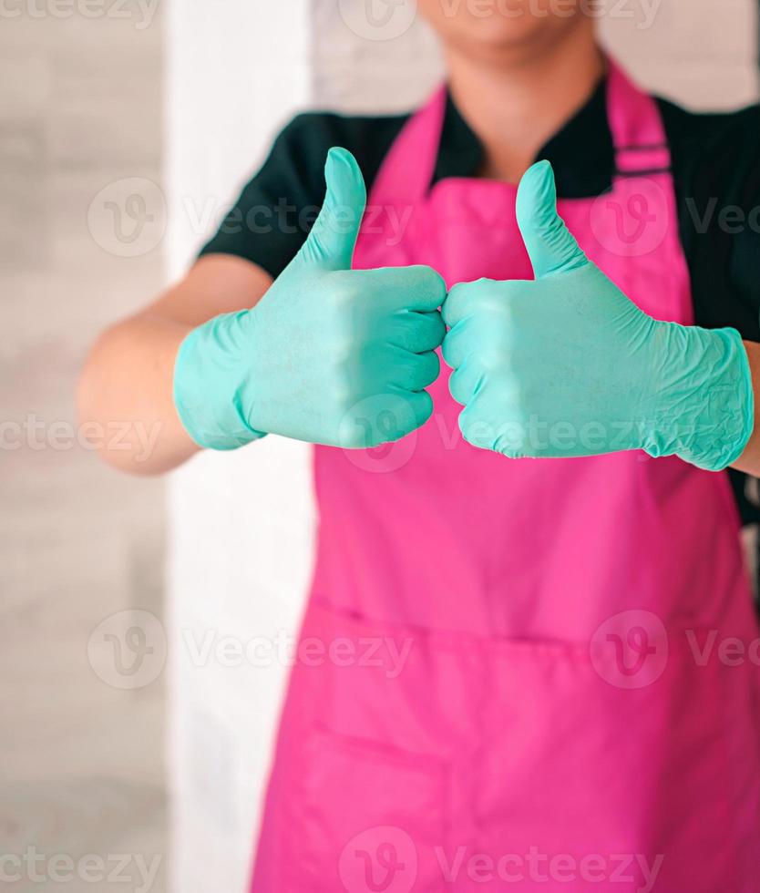 woman in latex gloves and pink apron holding thumbs up as a hope symbol. Ok, hope, win concept photo