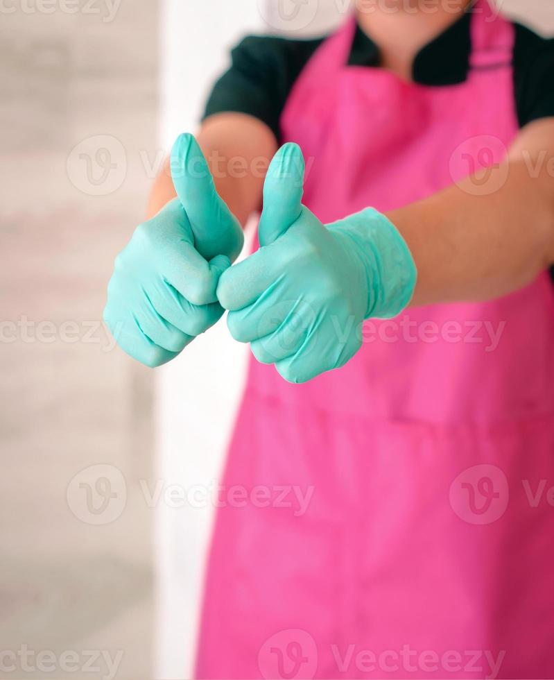 mujer con guantes de látex y delantal rosa levantando los pulgares como símbolo de esperanza. ok, espero, gane el concepto foto