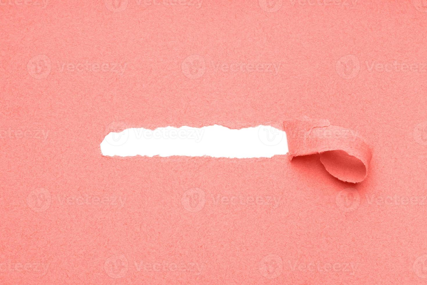 hole torn in coral color paper background to reveal hidden copy space photo