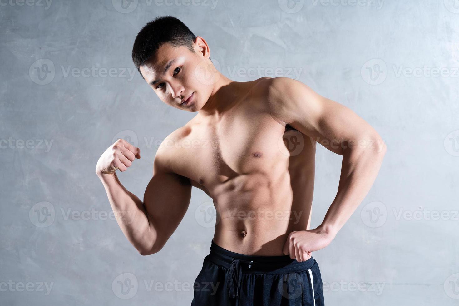 hombre asiático musculoso posando sobre fondo gris foto