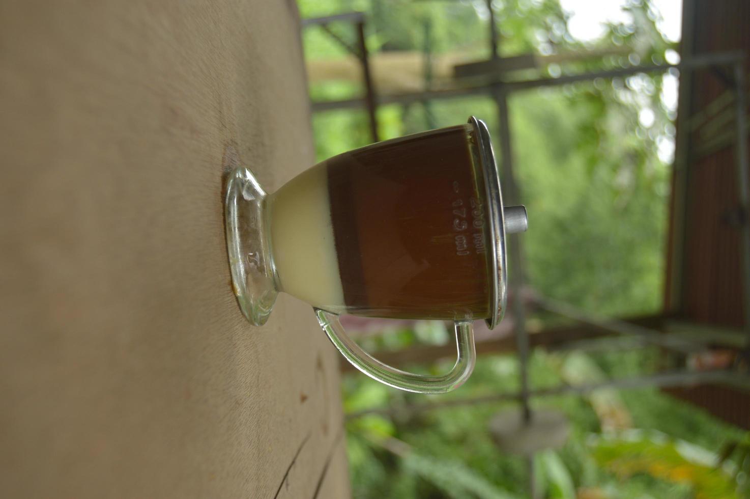 serving coffee with a clear glass and condensed milk underneath.  outdoor wooden background. photo