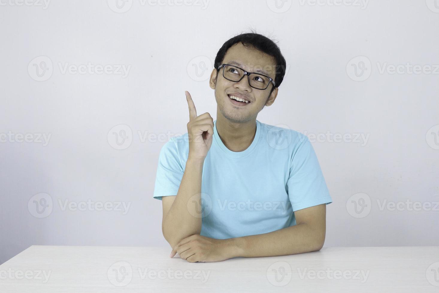 Young Asian man wear blue shirt and glasses with thinking and looking idea gesture in above empty space photo