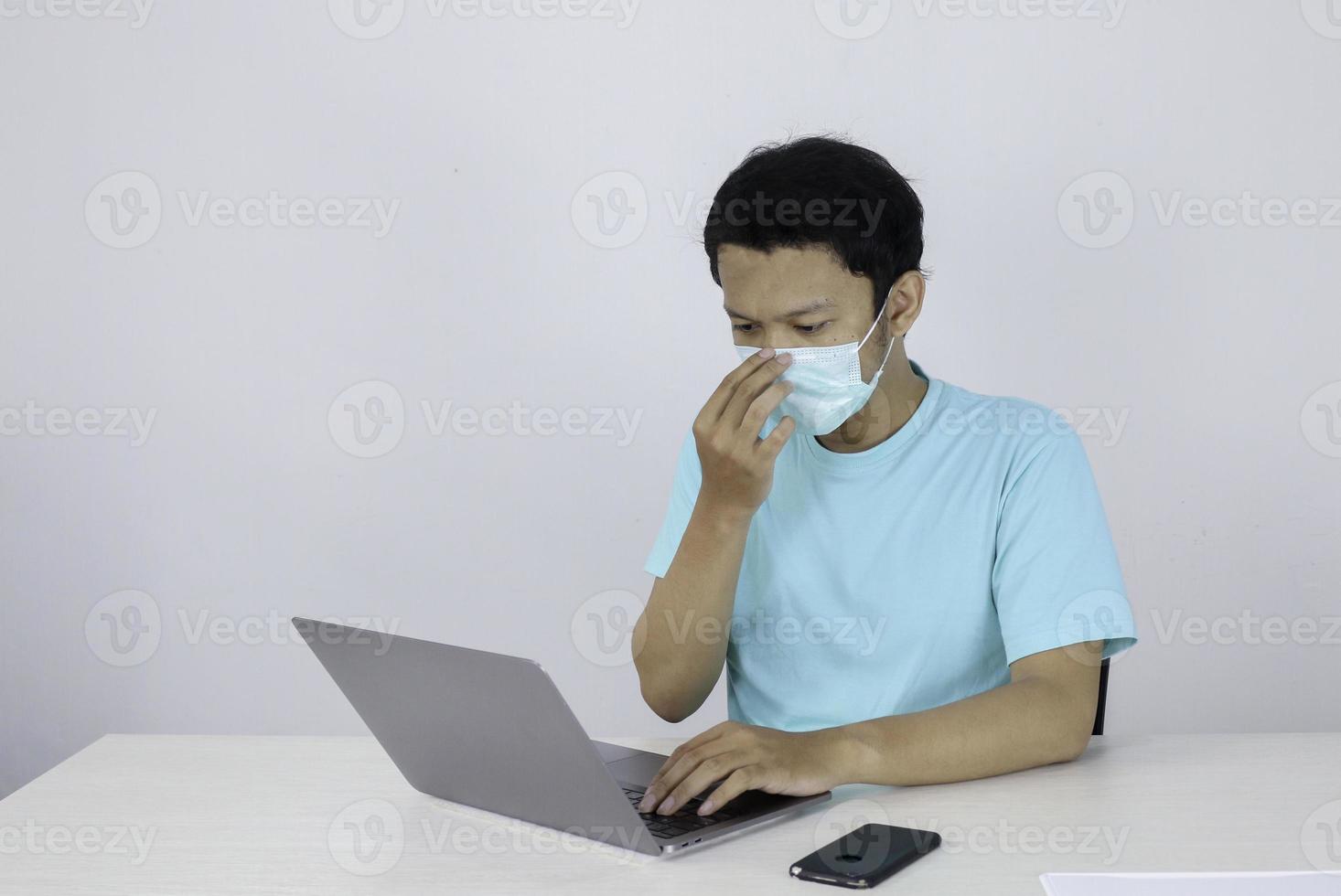 Young Asian man wear medical mask is cough when working with laptop on the table. photo