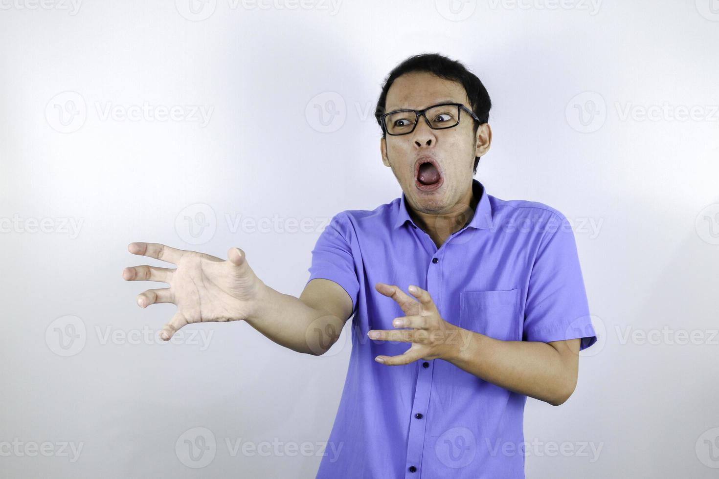 Young Asian Man wear blue shirt is funny angry face with shouting and pointing finger at camera isolated over white background photo
