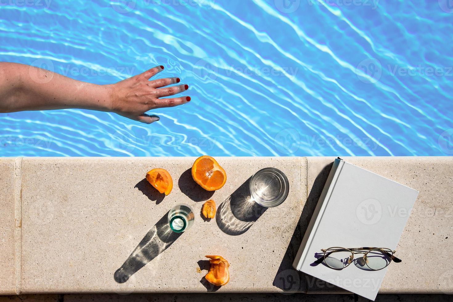 a hand into the water next to a white book with glasses and fruits photo