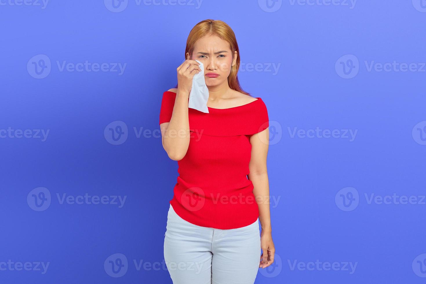 Portrait of sad woman she is crying wiping tears from eyes with tissue isolated on purple background photo