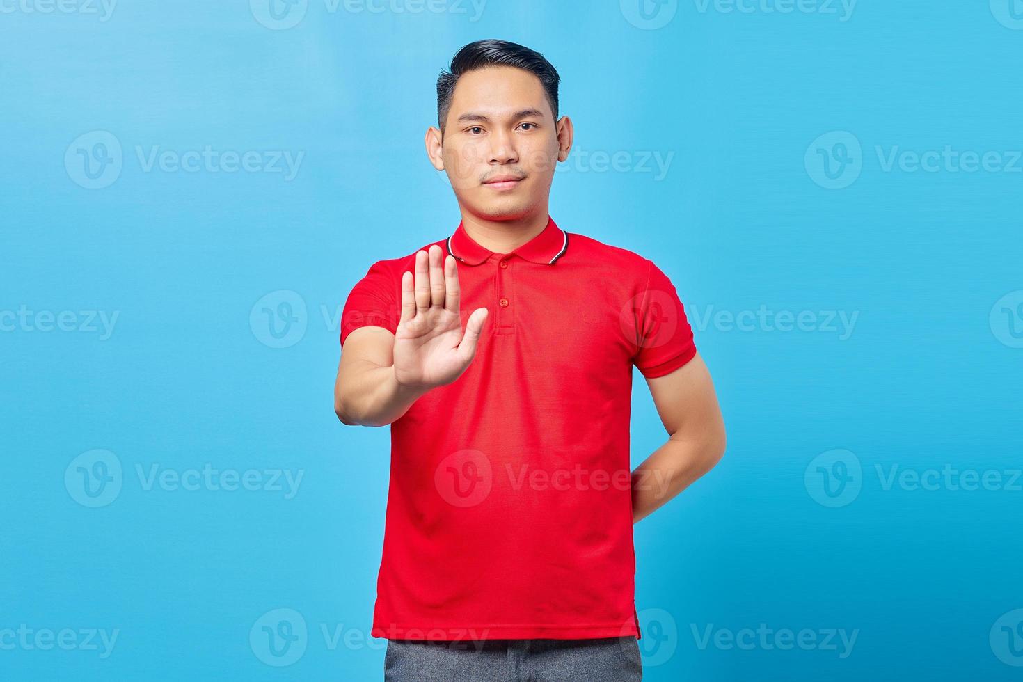 Portrait of annoyed young Asian man crossing hands makes stop gesture, demonstrates rejection isolated on blue background photo